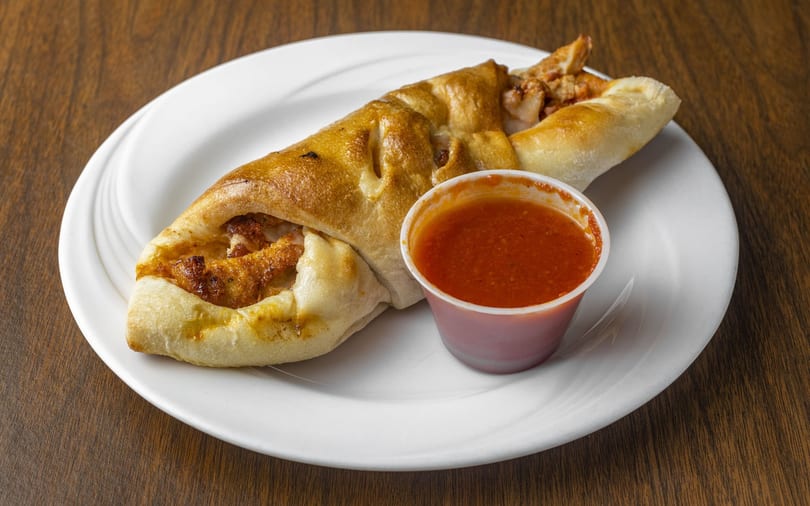 Golden-brown calzone filled with chicken and cheese, served with a side of marinara sauce.