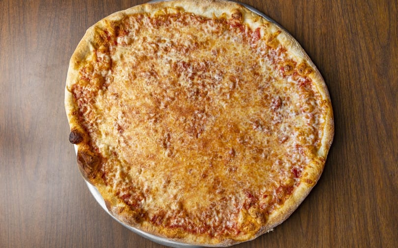 A large, round cheese pizza with a golden crust sits on a wooden table.