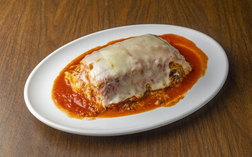 A large serving of lasagna with melted cheese and red sauce on a white oval plate.
